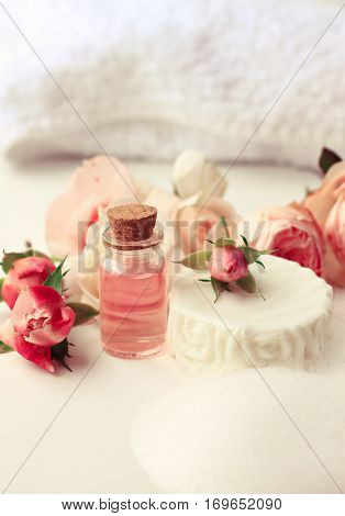 Rose aroma attar, white soap bar with foam, fresh pink garden flowers. Botanical skincare and aromatherapy. Vertical. Toned.