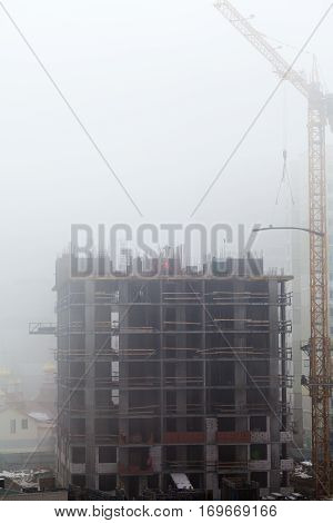 A new residential building under construction in the morning mist. Iron-concrete frame building. Builders in the formwork assembly.