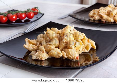 tasty pasta black large plate on the dining table. background the branch of tomatoes