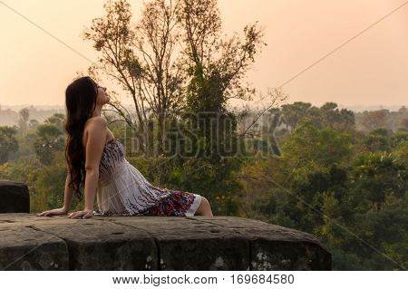 ANGKOR WAT CAMBODIA - JANUARY 28 2015: Young beautiful woman watching sunset at the top of Phnom Bakheng at Angkor Cambodia