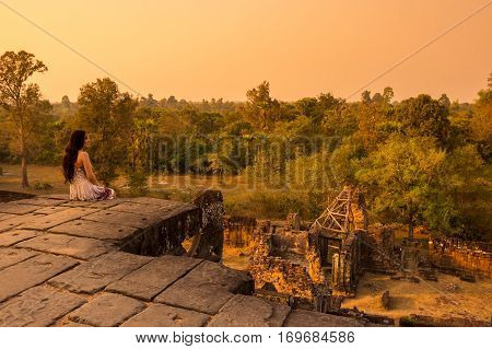 ANGKOR WAT CAMBODIA - JANUARY 28 2015: Young beautiful woman watching sunset at the top of Phnom Bakheng at Angkor Cambodia