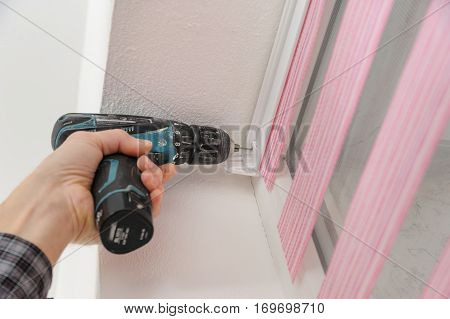 Installing fabric roller blinds. A man drilling holes to fix basis blinds.