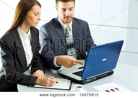 ein Mann verweist auf einen Bildschirm eines Laptops und eine Frau schaut