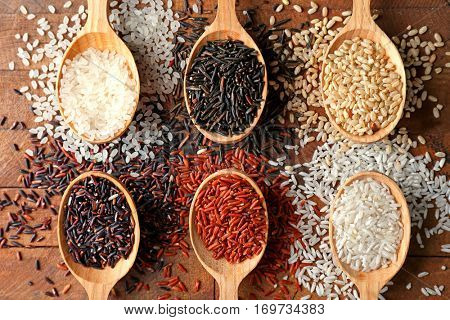 Different types of rice in spoons on wooden table, top view