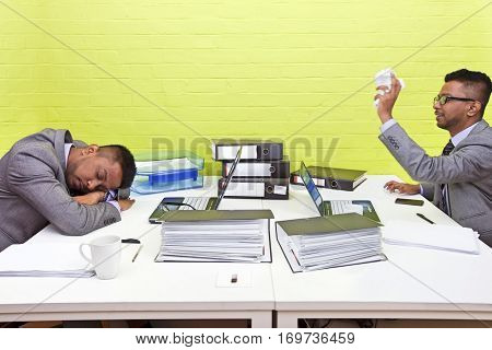 Indian businessman throwing paper at his sleeping twin