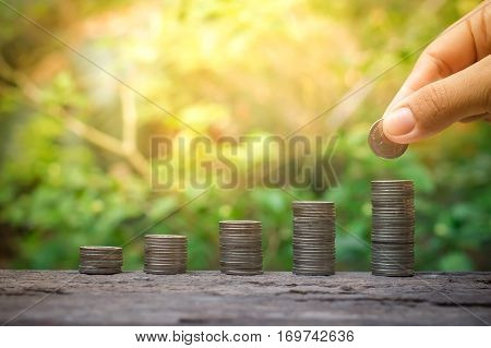 Close up of woman's hand putting coin stack of coins growing up for business investment or saving concept