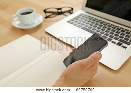 Hand holding smartphone above office table, closeup