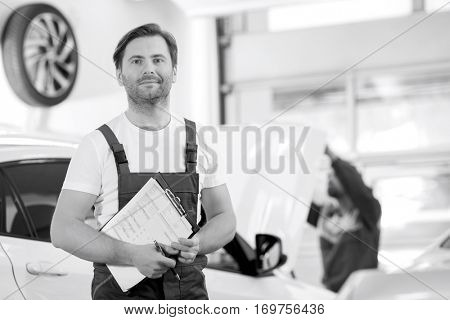 Portrait of confident male maintenance engineer with clipboard in car repair shop