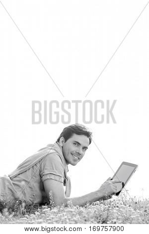 Side view portrait of young man using digital tablet while lying on grass against clear sky