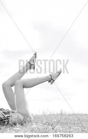 Low section of woman with feet up lying on grass against sky