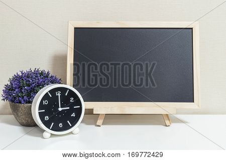 Closeup alarm clock for decorate show 3 o'clock with wood black board on white wood desk and cream wallpaper textured background selective focus at the clock