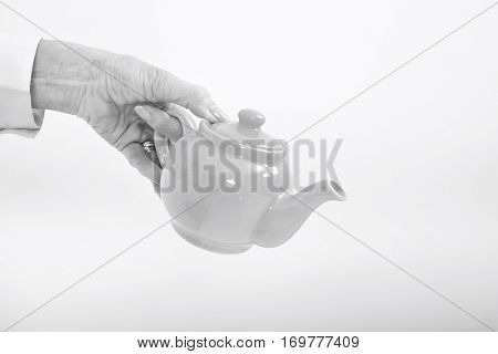 Senior businesswoman's hand holding teakettle over white background