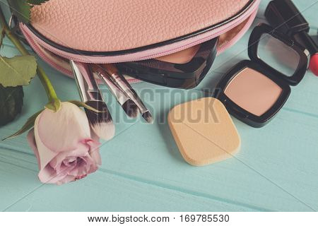 Cosmetic bag, rose and makeup products on wooden   background