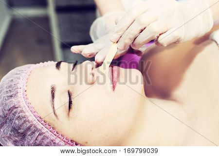Depilation with hot wax mustache in the beauty salon. Young woman receiving facial epilation close up. Cosmetologist removes hair on face. Beauty salon mustache depilation