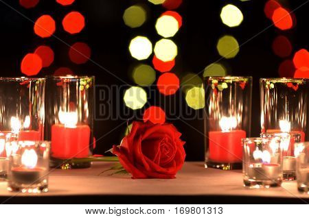 Beautiful red rose a concept of love and valentine's day put on a table with a candles in the glasses and blur enneagon yellow and red bokeh of light bulb in the backgroung in the night