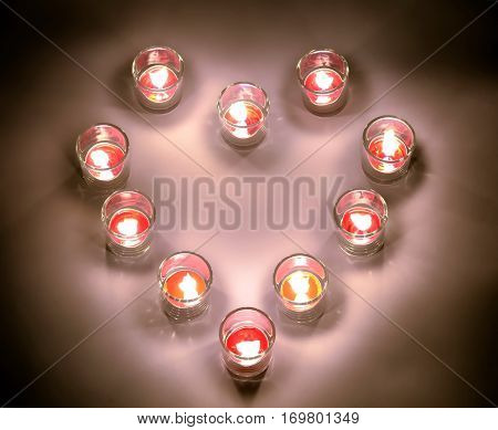 A small lighting lamps with red color aromatic paraffin in a small glasses arrange in heart form on a white floor in the night