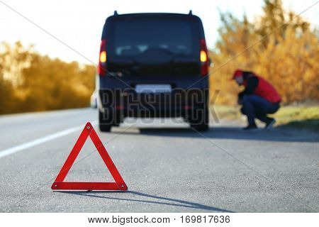 Red warning triangle on asphalt road. Driver near broken down car