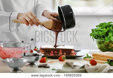 Cooking concept. Professional confectioner decorating delicious cake with chocolate frosting, closeup