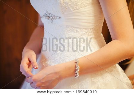 Elegant bridal white dress and young female hands with french manicure. Girl in luxury white wedding dress with bangle on wrist. Graceful stylish wedding gown with diamond breastpin. Brooch on gown