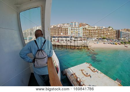 BARI, ITALY - JULY 13, 2016: thoughtful man with small backpack standing on ferry looking at Messina city skyline