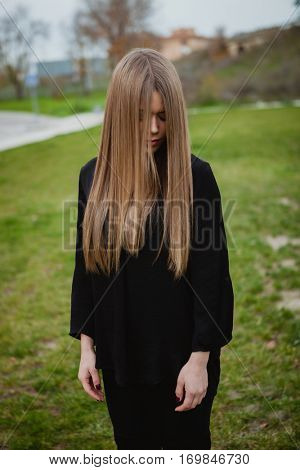 Blond girl with long blonde hair covering her face in the park