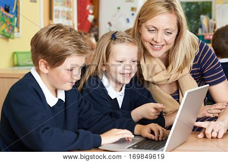 Teacher Helping Elementary School Pupils In Computer Class