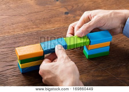 Person Hand Building Bridge Colorful Blocks At Wooden Desk