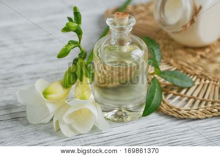 Spa still life with perfume and aromatic oil bottle surrounded by freesia flowers on light background