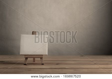 Blank art canvas on easel standing to left of frame on wood plank floor with empty wall behind and to the right.