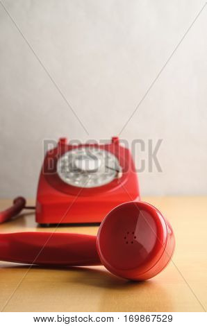 Eye level shot of a retro red 1960s to 70s British style telephone with receiver off the hook and in close up foreground. Dial base in soft focus background.