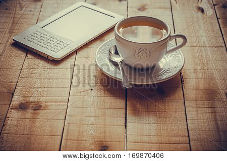 A cup of tea and an ebook reader on a rustic wood table by a window