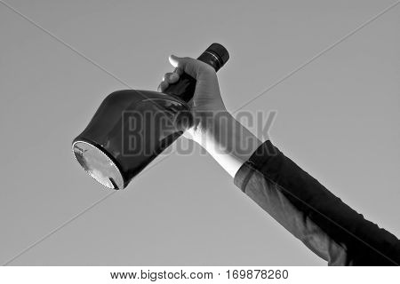 Human hand holding bottle of wine against blue sky. Concept of party.