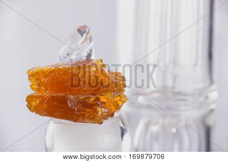 Piece of cannabis oil concentrate aka shatter over a glass rig isolated over white background