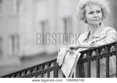 Thoughtful middle-aged woman holding map while leaning on railing