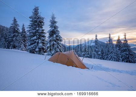 Yellow tent in the hoarfrost standing on an alpine meadow above the mountain valleys covered with mist during magic winter dawn. Winter expedition.