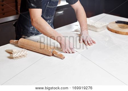Roll out the dough. Closeup hand of chef baker in uniform blue apron cook pizza at kitchen.