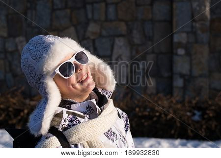 Funny little girl in sunglasses in winter a sunny day. Caucasian stylish little girl in winter clothes walking outdoor. Pretty charming little girl. Portrait of little fashion kid girl .