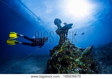 Free diver exploring the underwater statue in a tropical sea