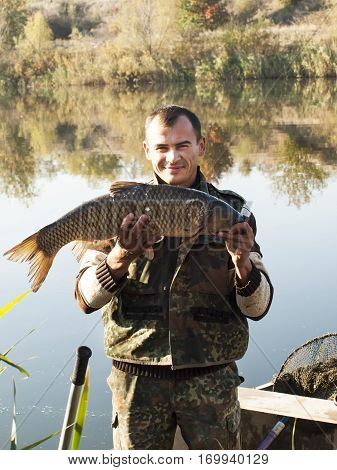 Fisherman With fish Mirror Carp. Fishing on river on autumn