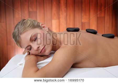 Blond kvinde håndspålæggelsen massage seng med varme sten