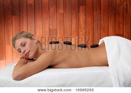 Blond kvinde håndspålæggelsen massage seng med varme sten