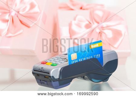 Wireless payment terminal with credit or debit card at shop with gifts in the background 