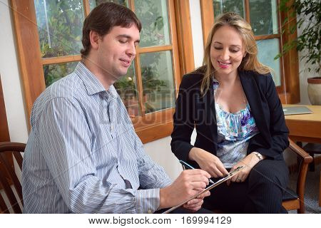 Two business colleagues, young successfull man and attractive elegant woman, discussing some project, talking over document, sitting in the office.