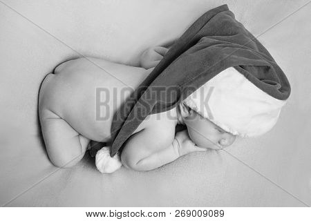 A Naked Newborn Baby Sleeps In A Christmas Hat.