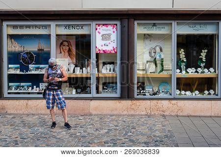 Leoben, Styria, Austria - August 06, 2018: The Man Stands On The Sidewalk At The Shop Window And Loo