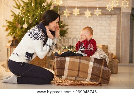Mother Comforts Her Little Crying Son On Background Of The Christmas Tree And Festive Garlands.