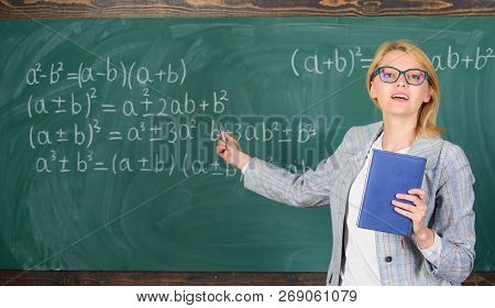 Teacher Smart Woman With Book Explain Topic Near Chalkboard. School Teacher Explain Things Well And 