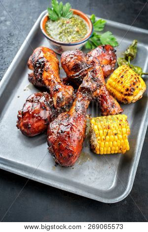 Traditional barbecue chicken drumsticks with corn and chimichurri sauce as top view in a silber fryer 