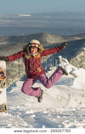 Snowboarder Girl Freerider Is Jump In The Snowy Mountains In Winter Under The Clouds