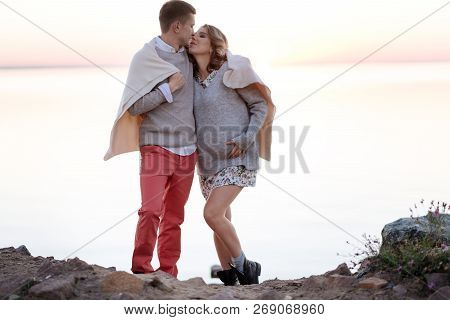 Young Family Expecting A Baby Walking Together Covered With A Plaid
